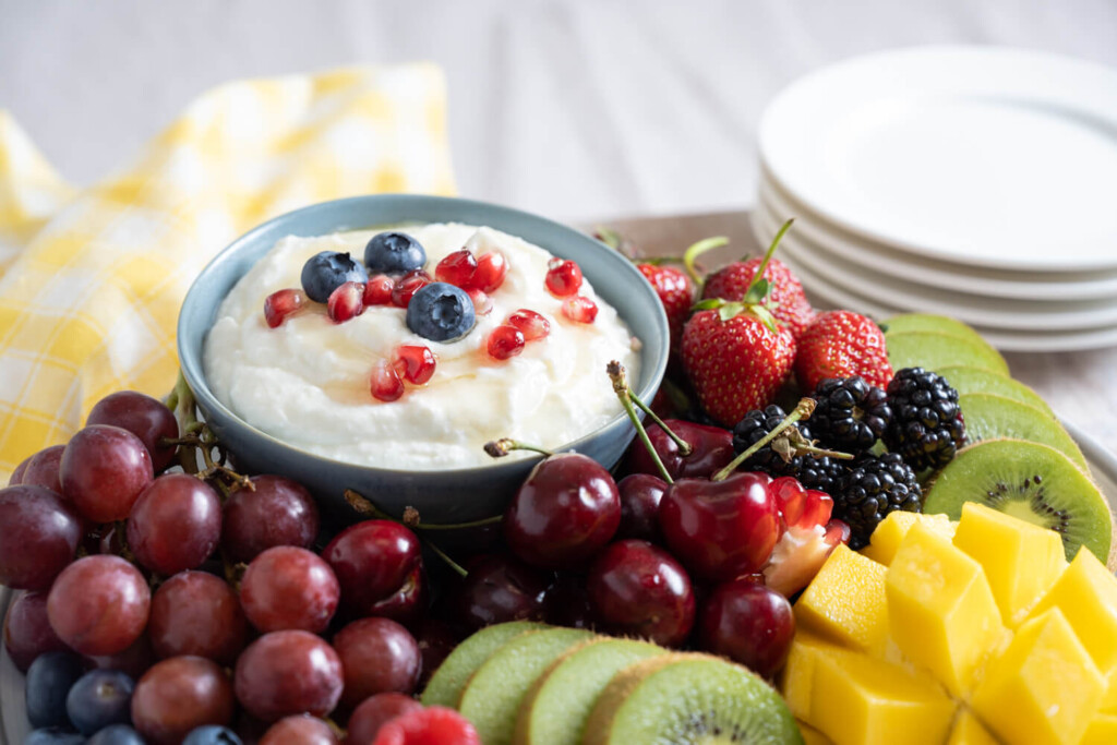 Plate of assorted fruit with bowl of whipped ricotta garnished with blueberries and pomegranate seeds
