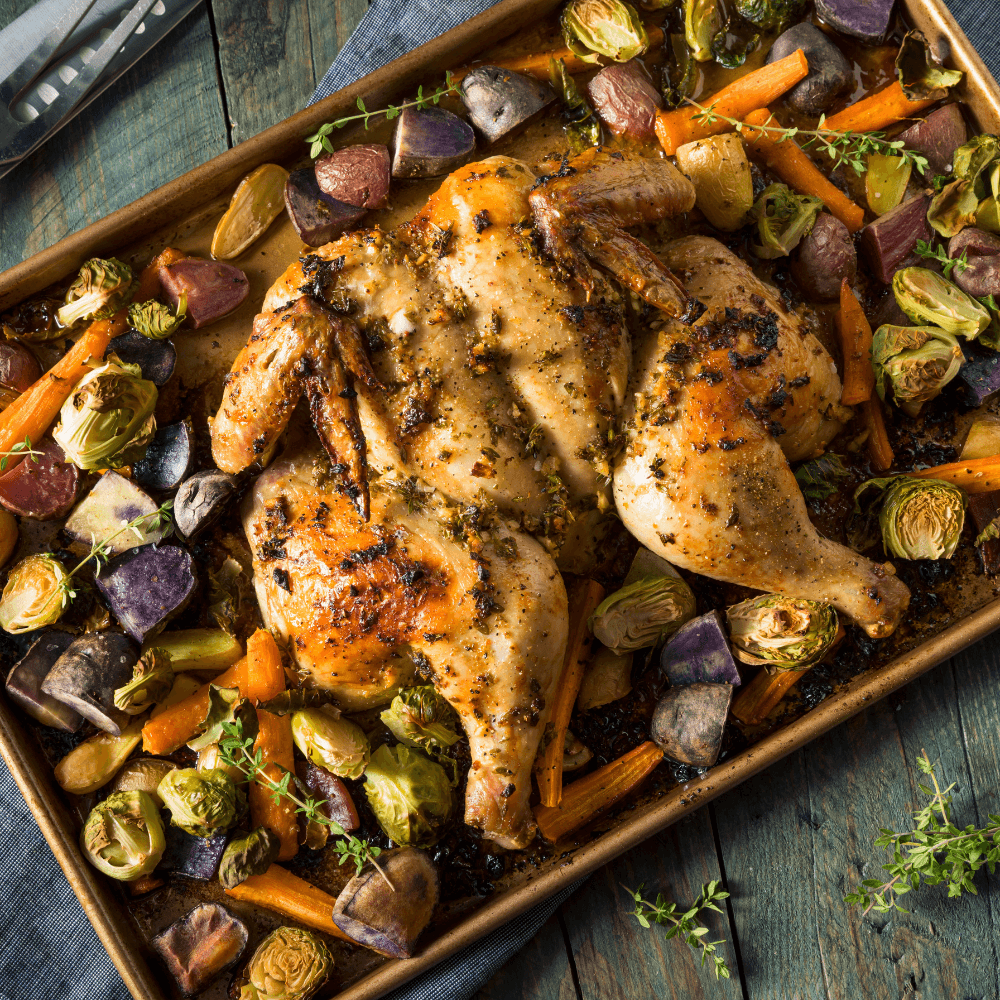Stock image of roasted flattened chicken on baking sheet surrounded by roasted root vegetables.