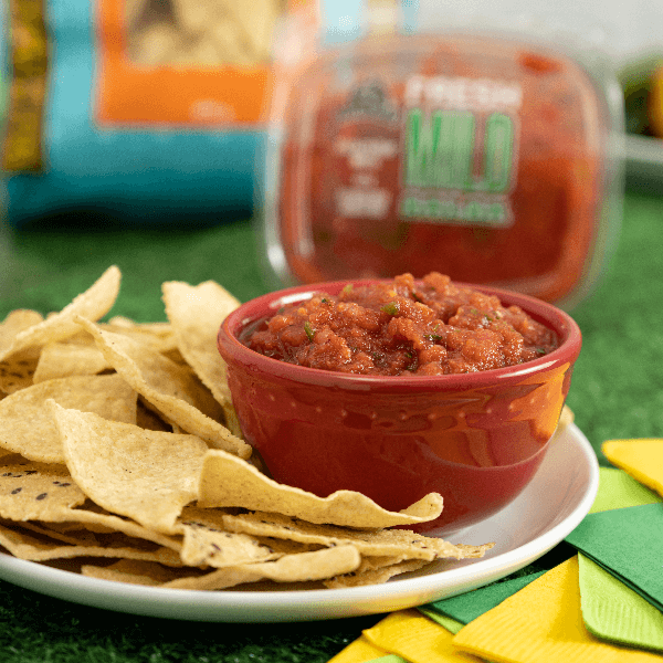Red bowl of fresh salsa on a plate with tortilla chips.
