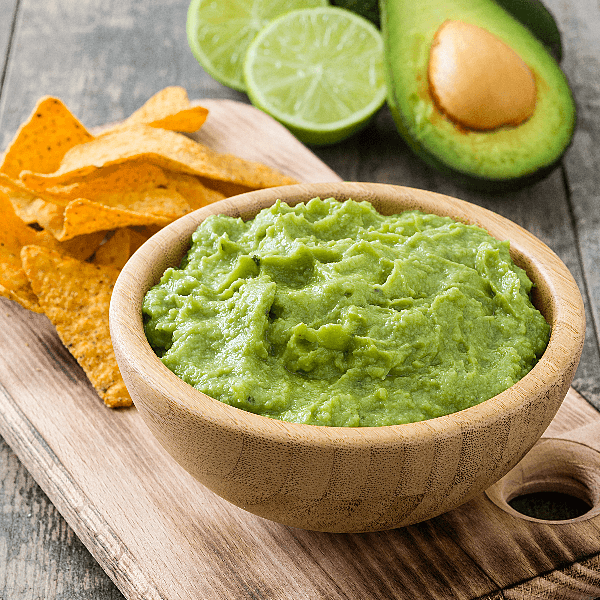 Stock image of wooden bowl of guacamole on wooden serving tray.