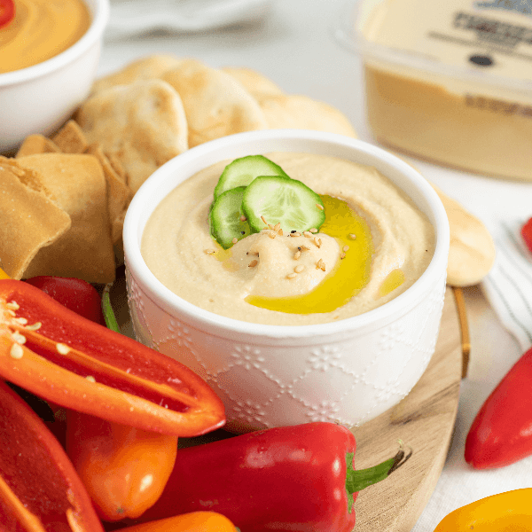 White bowl of hummus garnished with olive oil and cucumber coins.