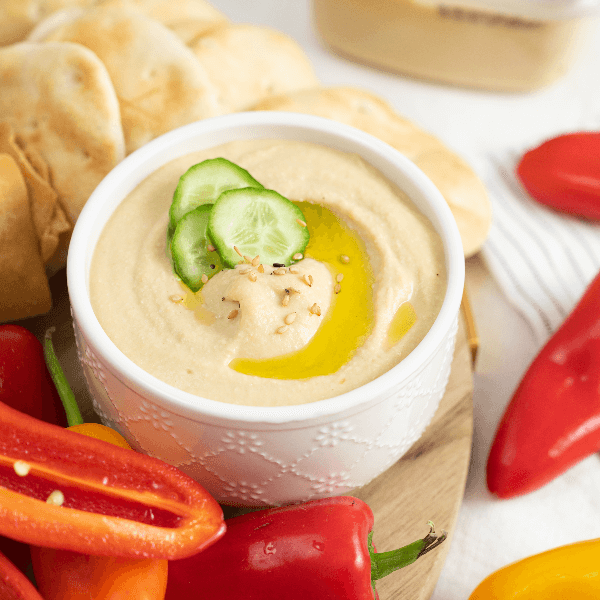 Bowl of hummus garnished with olive oil, sesame seeds, and cucumber coins