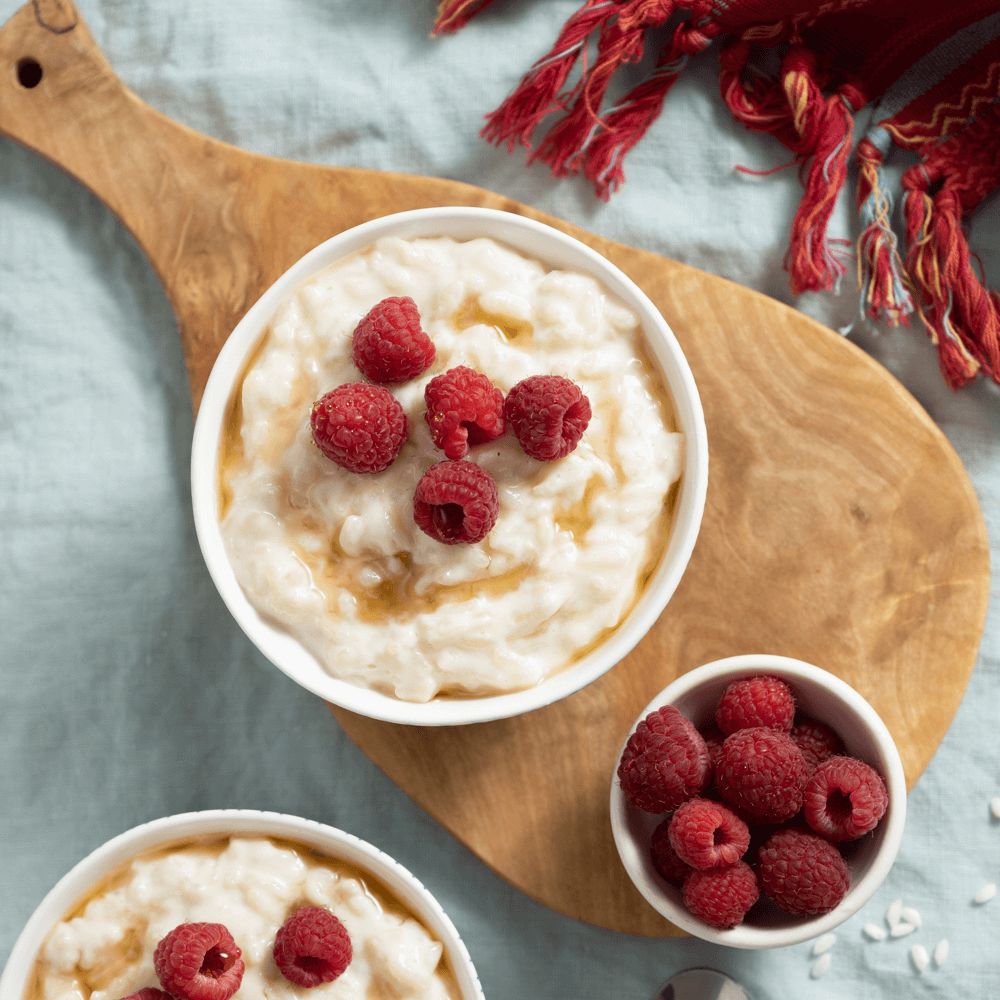 Overhead image of a bowl on a wooden cutting board flled with maple rice pudding garnished with fresh raspberries.