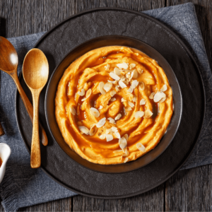 vanilla bean whipped sweet potatoes with maple syrup and almond flakes in black bowl on dark wooden table with ingredients, horizontal view from above, flat lay