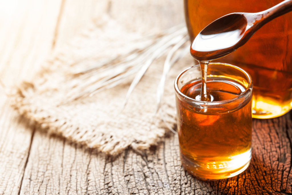 Glass jar of maple syrup with wooden spoon on table.