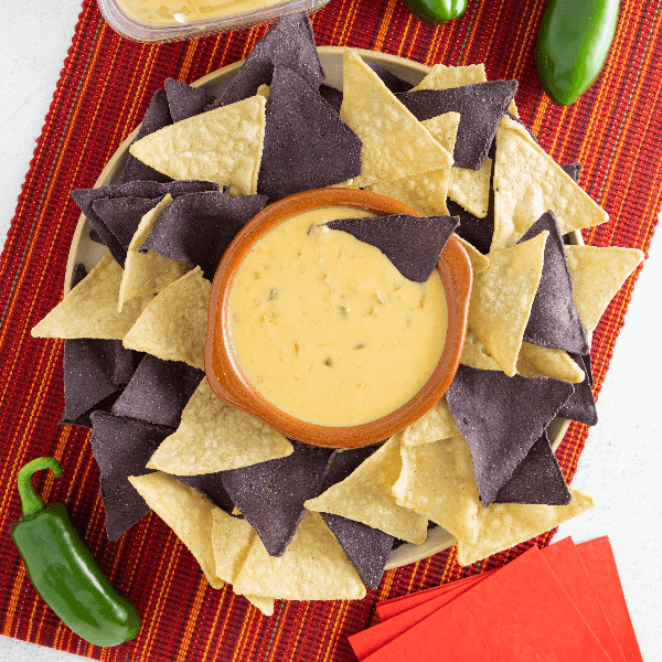 Overhead image of plate with blue and white corn tortilla chips and red bowl of queso in the centre.