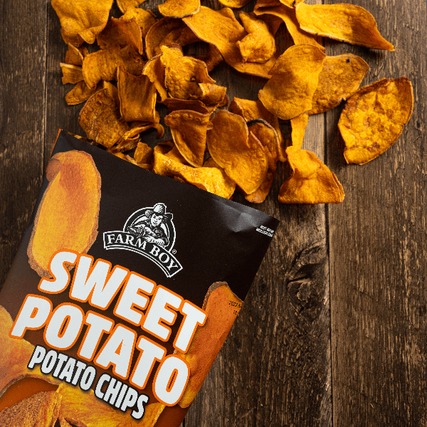 Bag of open Farm Boy Sweet Potato Chips on wooden table with chips spilling out.