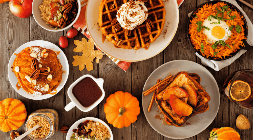 Autumn breakfast or brunch buffet table scene against a dark wood background. Pumpkin spice, waffles, pancakes, apple french toast, oatmeal, egg skillet, yogurt. Overhead view.