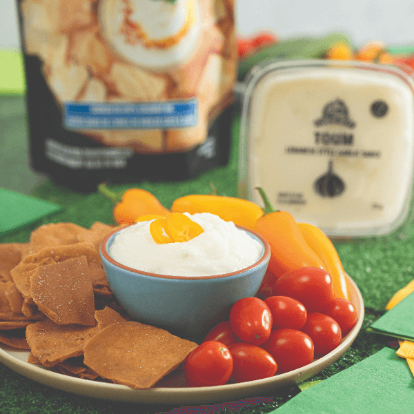 Plate with veggies and chips and a bowl of toum in the centre.