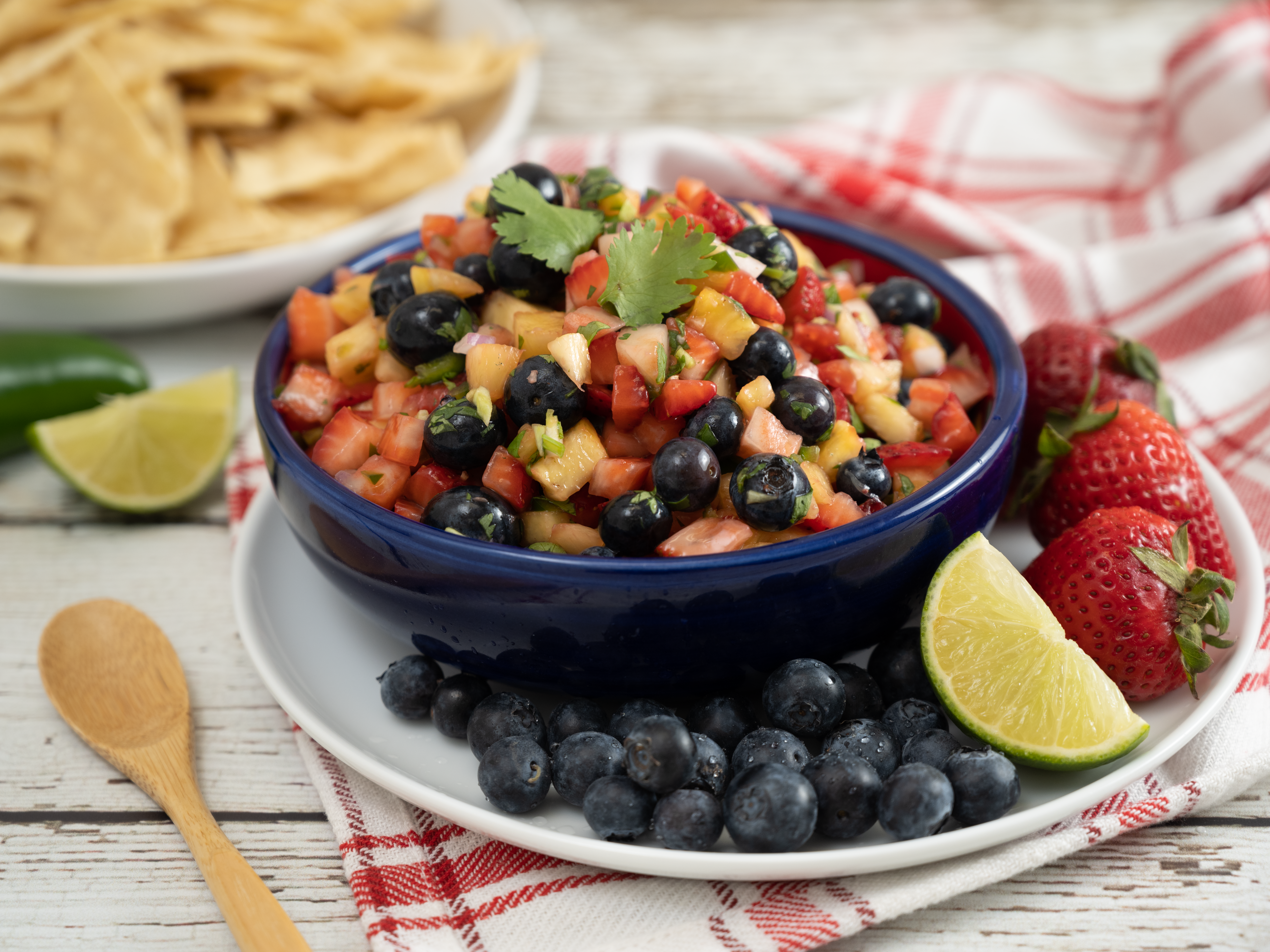 A sweet and tangy berry fruit salsa served in a bowl on a plate along with blueberries and strawberries on the side. 