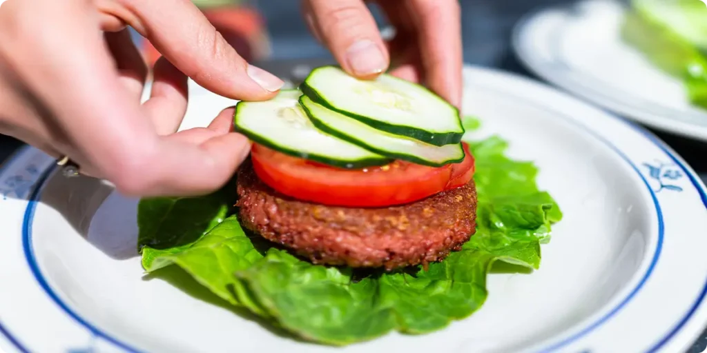 A pair of hands arranging the product or veggie toppings on a burger